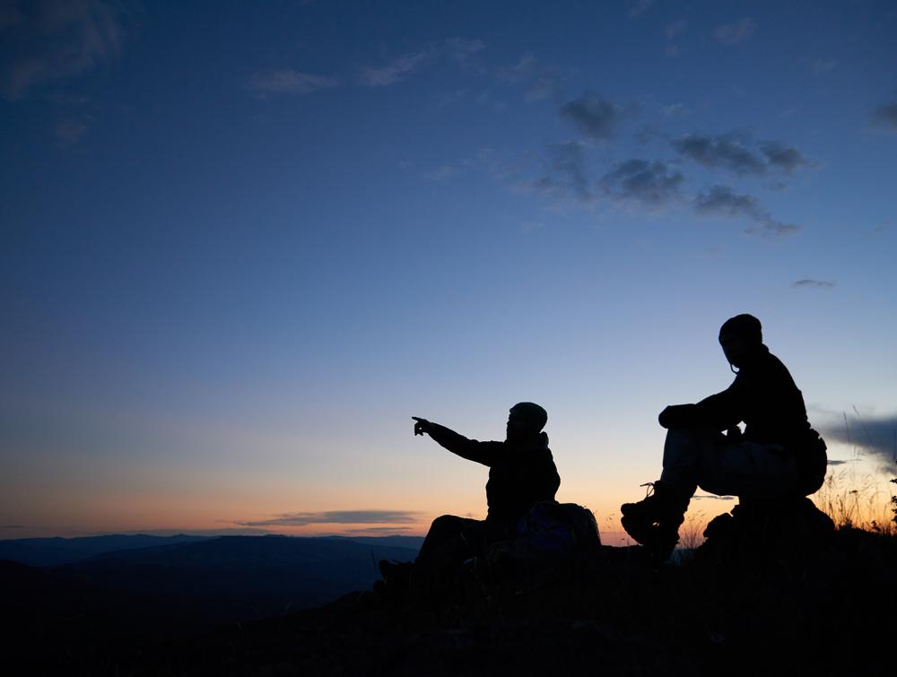 silhouettes of two people looking at the horizon, with one of them pointing 