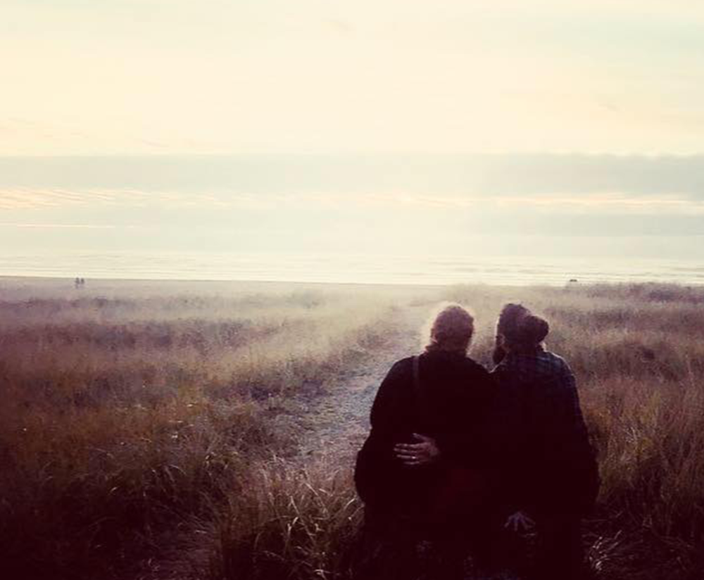 the backs of two people embracing during a sunset on a beach