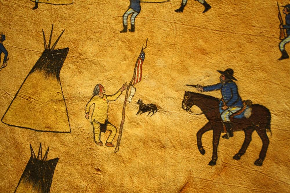 painted image of cavalryman on horseback, pointing gun at a Native American