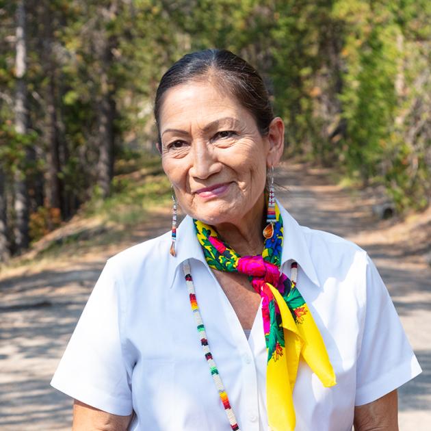 Interior Secretary Deb Haaland smiling in front of a forest.