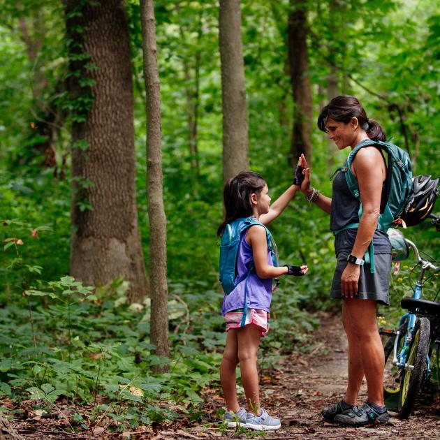 A woman and child high five during a break from bicycling along a forested trail