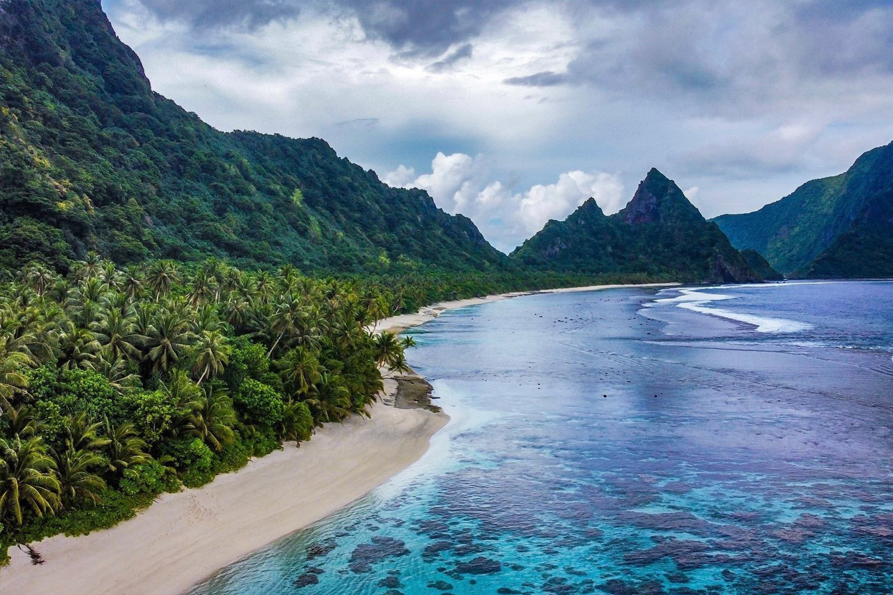 Beach with corals surrounded by high tropical mountains