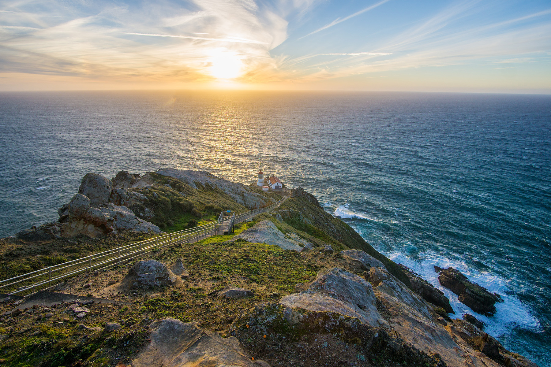 view of sunset over pacific ocean from up a hill overlooking a lighthouse as well