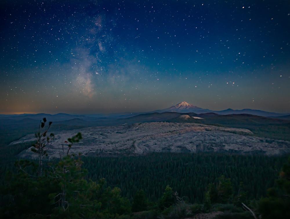 A wide view of a starry night sky over Sáttítla (Medicine Lake Highlands) in California.