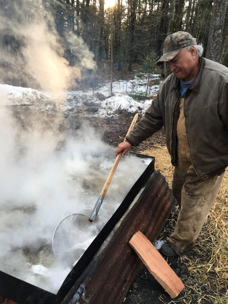 A man skims off foam from the top of the sap boil. 