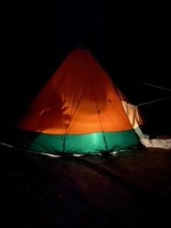An orange and green tent glows brightly in the night.