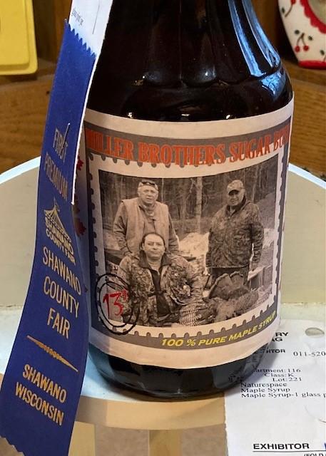 A bottle of syrup with three men on the wrap, with a first place blue-ribbon on it.