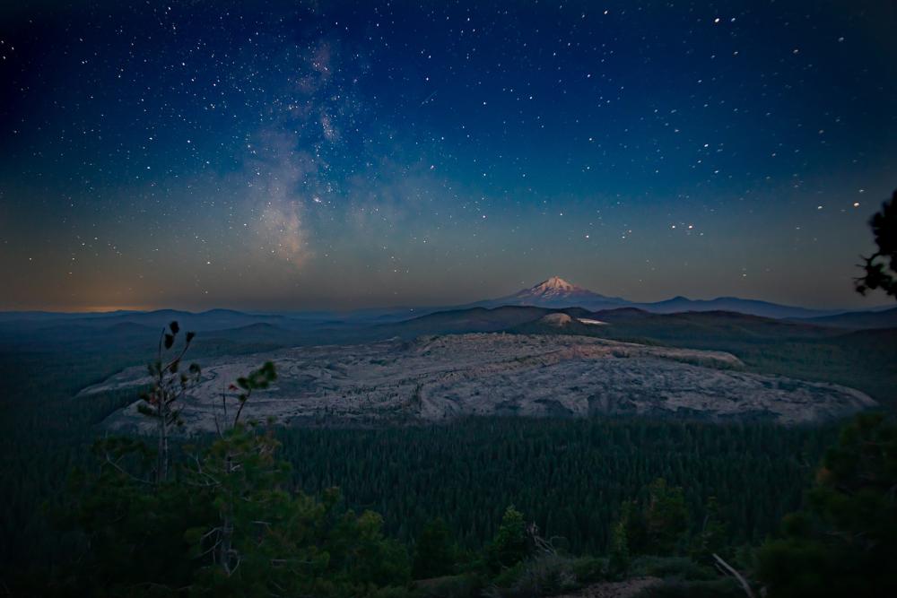 A wide view of a starry night sky over Sáttítla (Medicine Lake Highlands) in California.