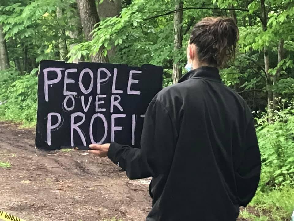 A woman stands holding a sign that reads: 'People Over Profit'