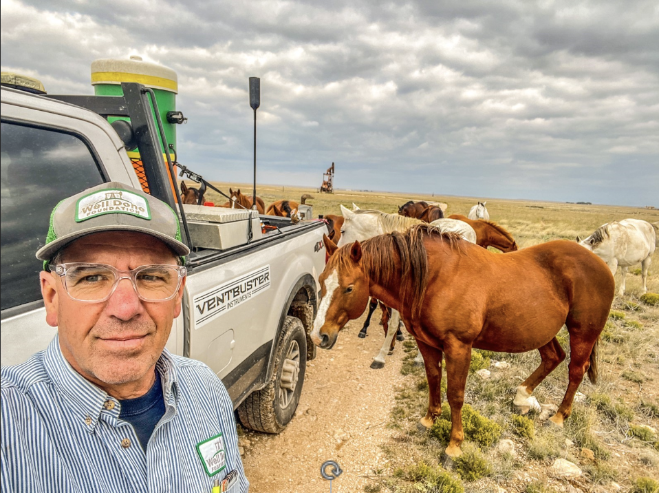 a white man poses next to a truck outside near horses