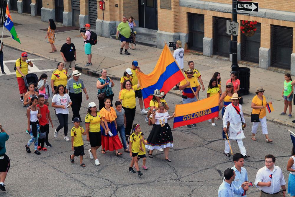 aerial view of a few people marching down the street with Colombian flags and dressed with Colombian outfits