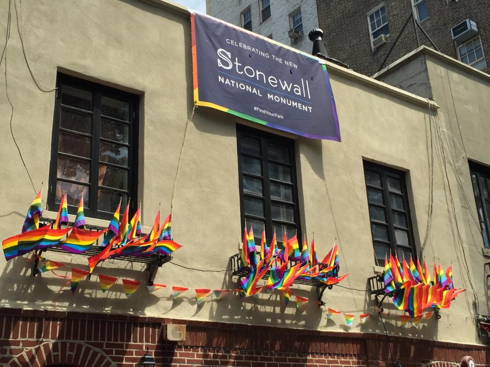 Facade of brick building with banner reading "Celebrating the new Stonewall National Monument" and a row of small rainbow flags