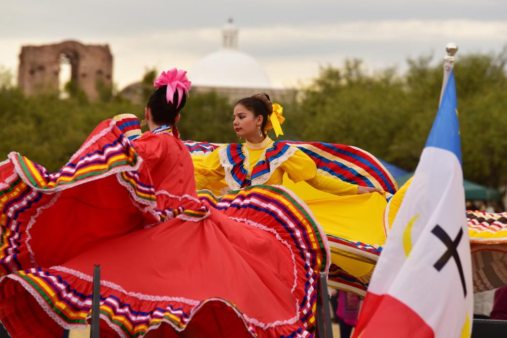 two women with colorful mexican folklore dresses dancing with the ruins of a church in the background