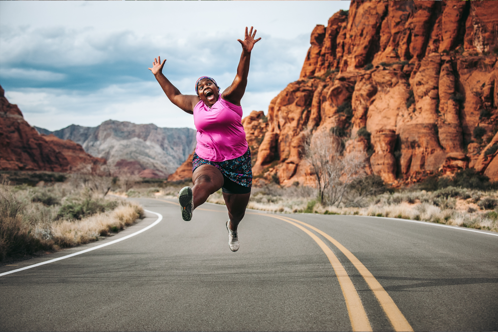 person happily jumping while running on a street surrounded by canyons