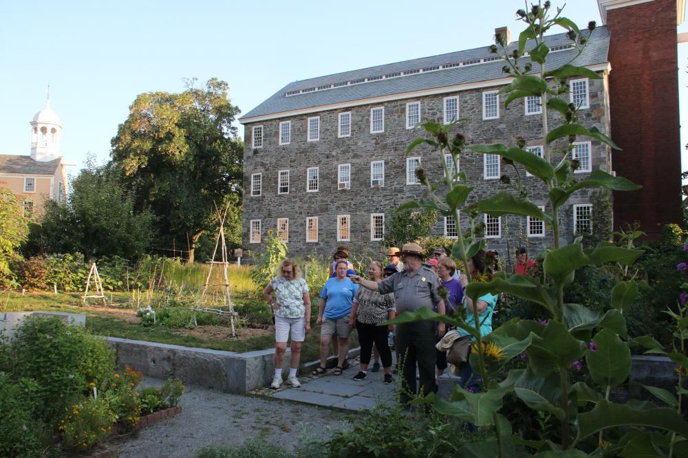 ranger pointing at flowers while giving a tour, with a mill in the back