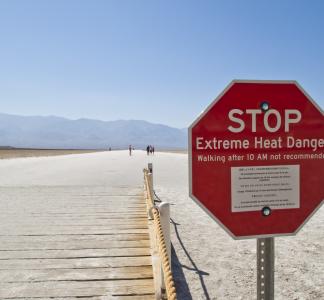 stop sign in the desert that says "extreme heat caution" 